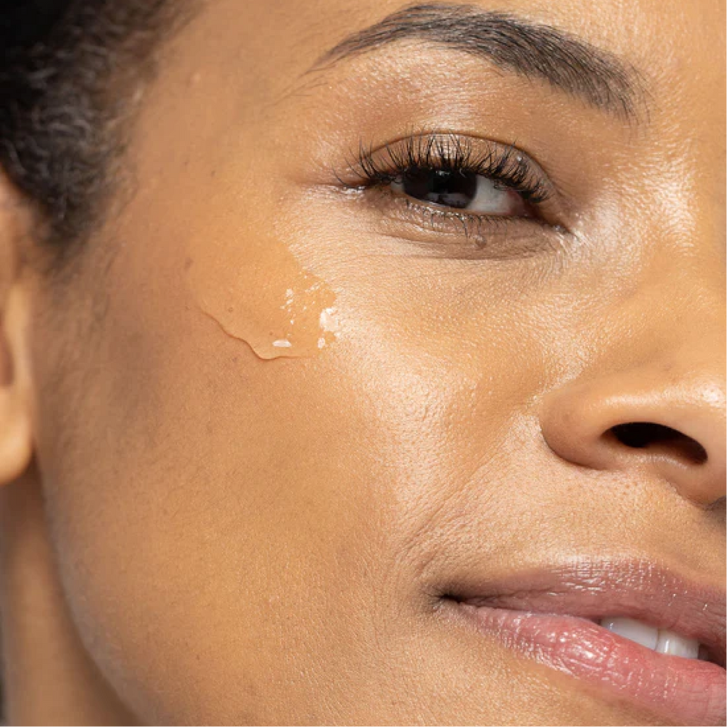 Close-up image of a person's cheek with a dab of Vivier HEXAM Gentle Gel Cleanser. The cleanser appears as a translucent gel on the skin, subtly reflecting light. The person's skin is visible around the gel, emphasizing the application process. The background is soft-focused to highlight the action on the face.