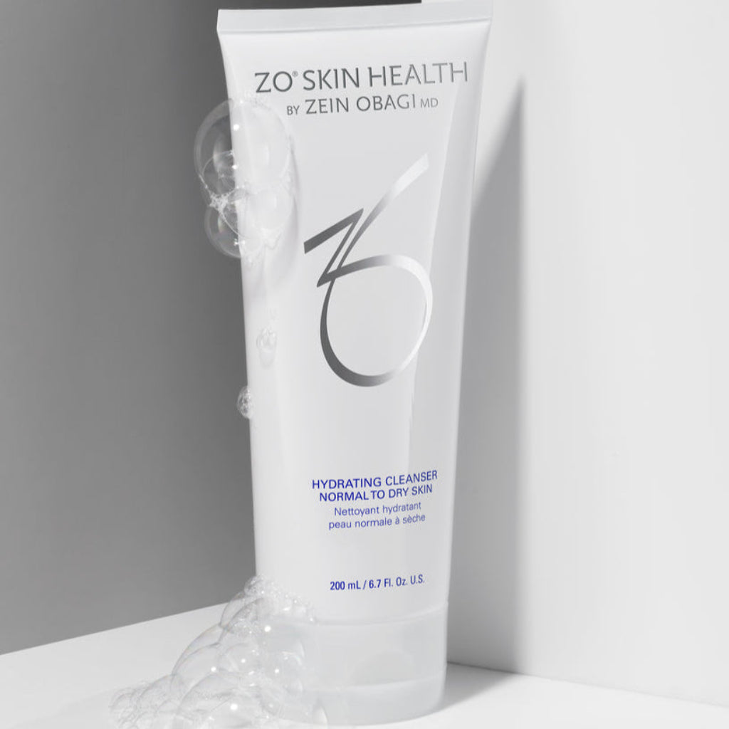 ZO Skin Health Hydrating Cleanser tube with silver and blue branding, surrounded by bubbles, against a sleek white and gray background