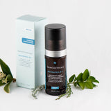 SkinCeuticals Resveratrol B E serum bottle displayed beside a flower, highlighting its antioxidant-rich formula for overnight skin renewal and radiance.