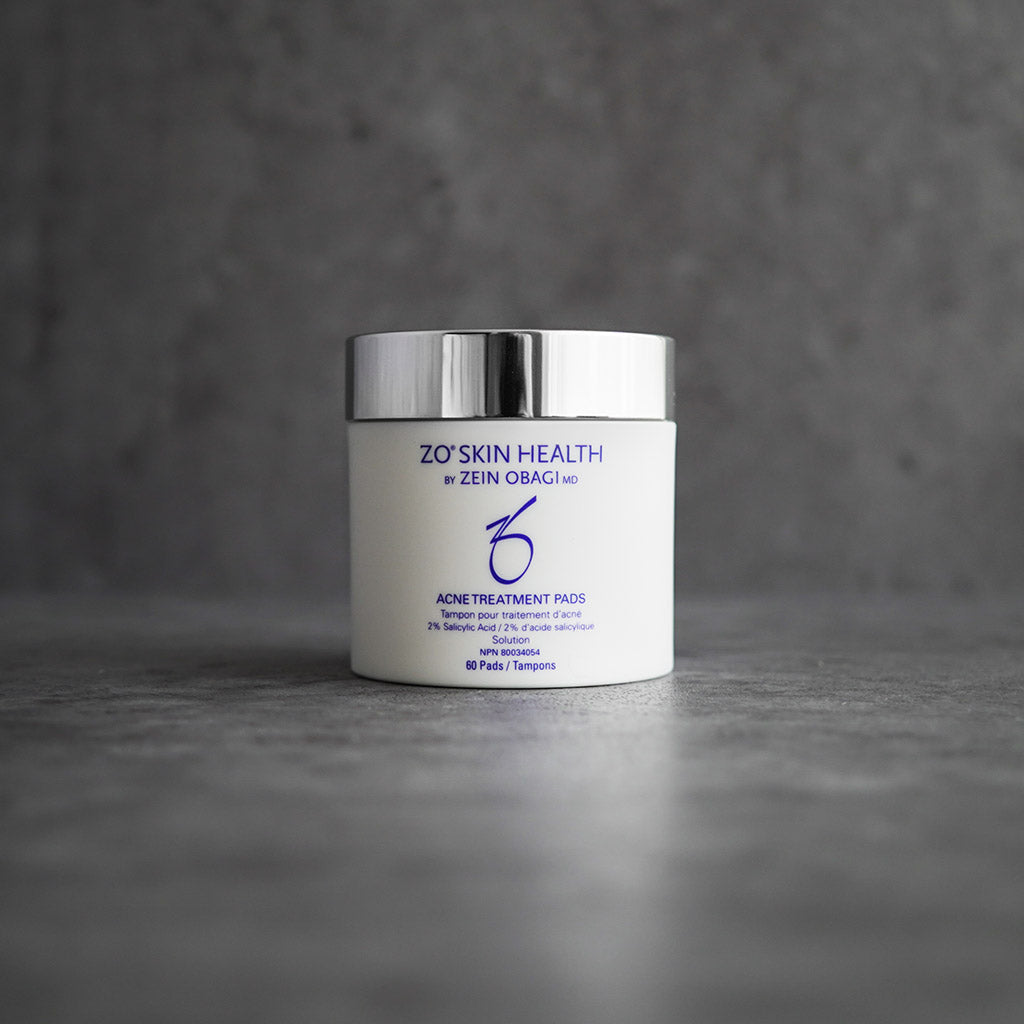 ZO Skin Health Acne Treatment Pads 60-count jar displayed on a grey concrete background, featuring 2% salicylic acid formula to treat acne, control oil, and minimize pores