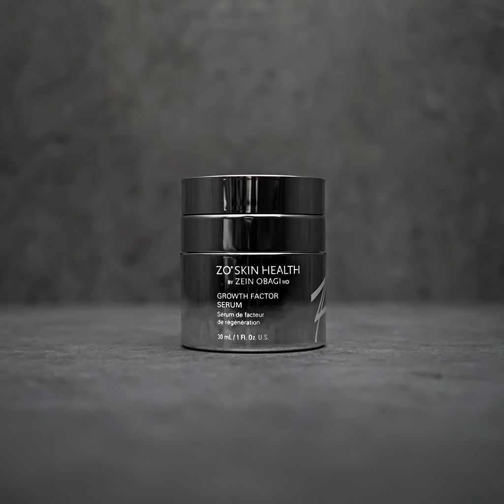 Stylish product image of ZO Growth Factor Serum (30ml) presented against a sophisticated grey background, showcasing the elegant silver and blue packaging of this lightweight serum designed to firm skin, smooth wrinkles, and enhance elasticity
