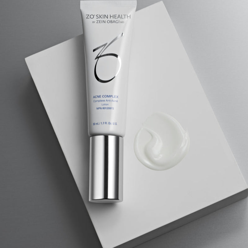 Product image of ZO® Acne Complex placed on top of a white box, with a visible swatch of the lightweight treatment beside it, highlighting its smooth texture and advanced formula designed to treat breakouts, prevent future acne, and improve post-acne marks and skin texture