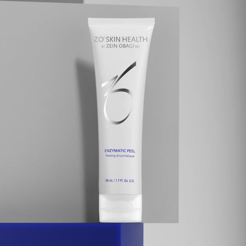 Product image of ZO Enzymatic Peel (50ml) placed on a blue countertop with a clean white wall background, showcasing its elegant silver and white packaging designed for gentle at-home resurfacing, hydration, and brightening.