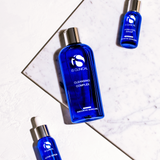Three blue skincare bottles from the brand 'iS Clinical' on a marble surface.