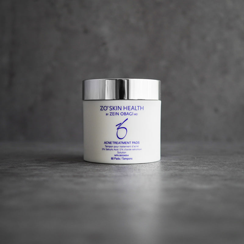 ZO Skin Health Acne Treatment Pads 60-count jar displayed on a grey concrete background, featuring 2% salicylic acid formula to treat acne, control oil, and minimize pores