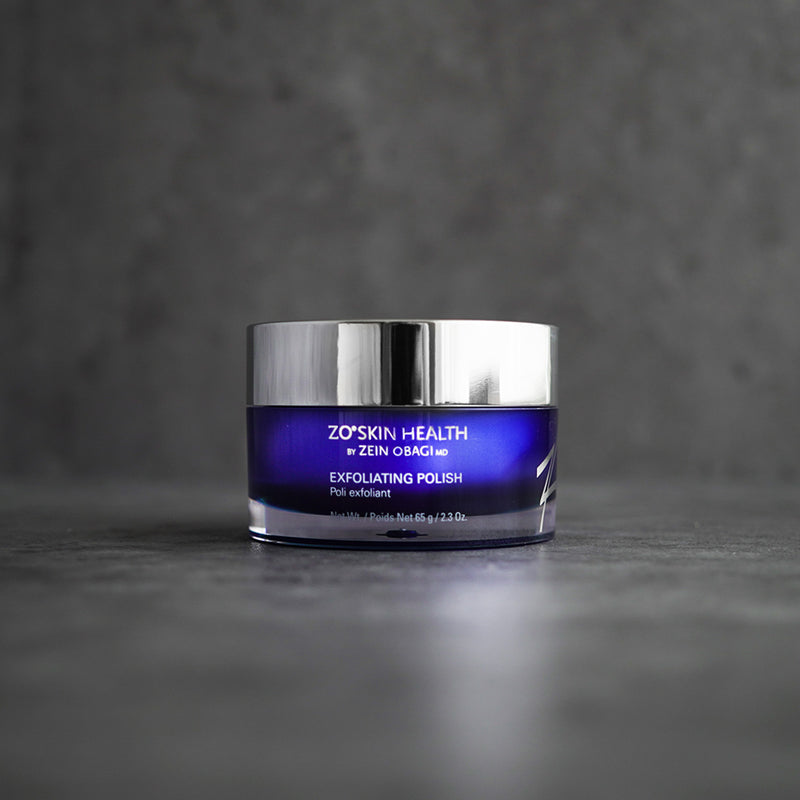 ZO Skin Health Exfoliating Polish 65g jar displayed on a grey concrete background, highlighting the luxurious packaging and exfoliating formula with magnesium crystals for radiant skin