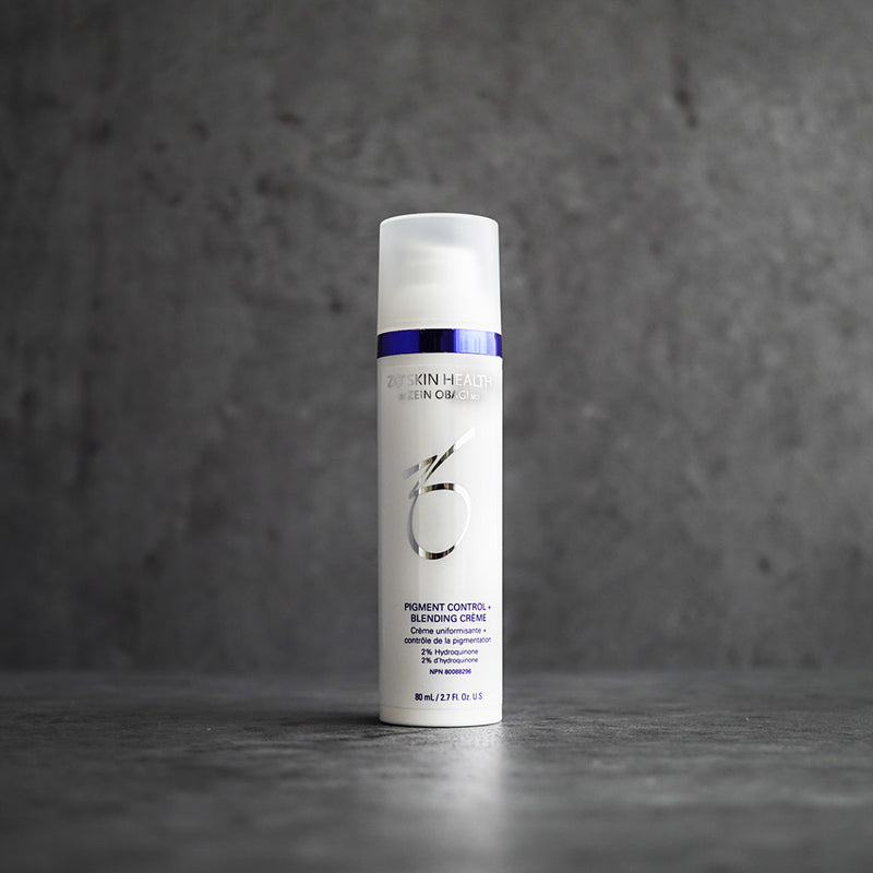 Product image of ZO® Pigment Control + Blending Crème 2% HQ placed on a grey concrete background, showcasing its sleek silver and white packaging, designed to target hyperpigmentation, melasma, and uneven skin tone for a brighter, more balanced complexion.