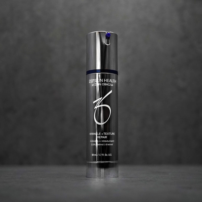 Stylish product image of ZO Wrinkle + Texture Repair crème placed against a dark grey concrete background, showcasing its luxurious silver and blue packaging designed to smooth wrinkles, improve texture, and rejuvenate skin tone
